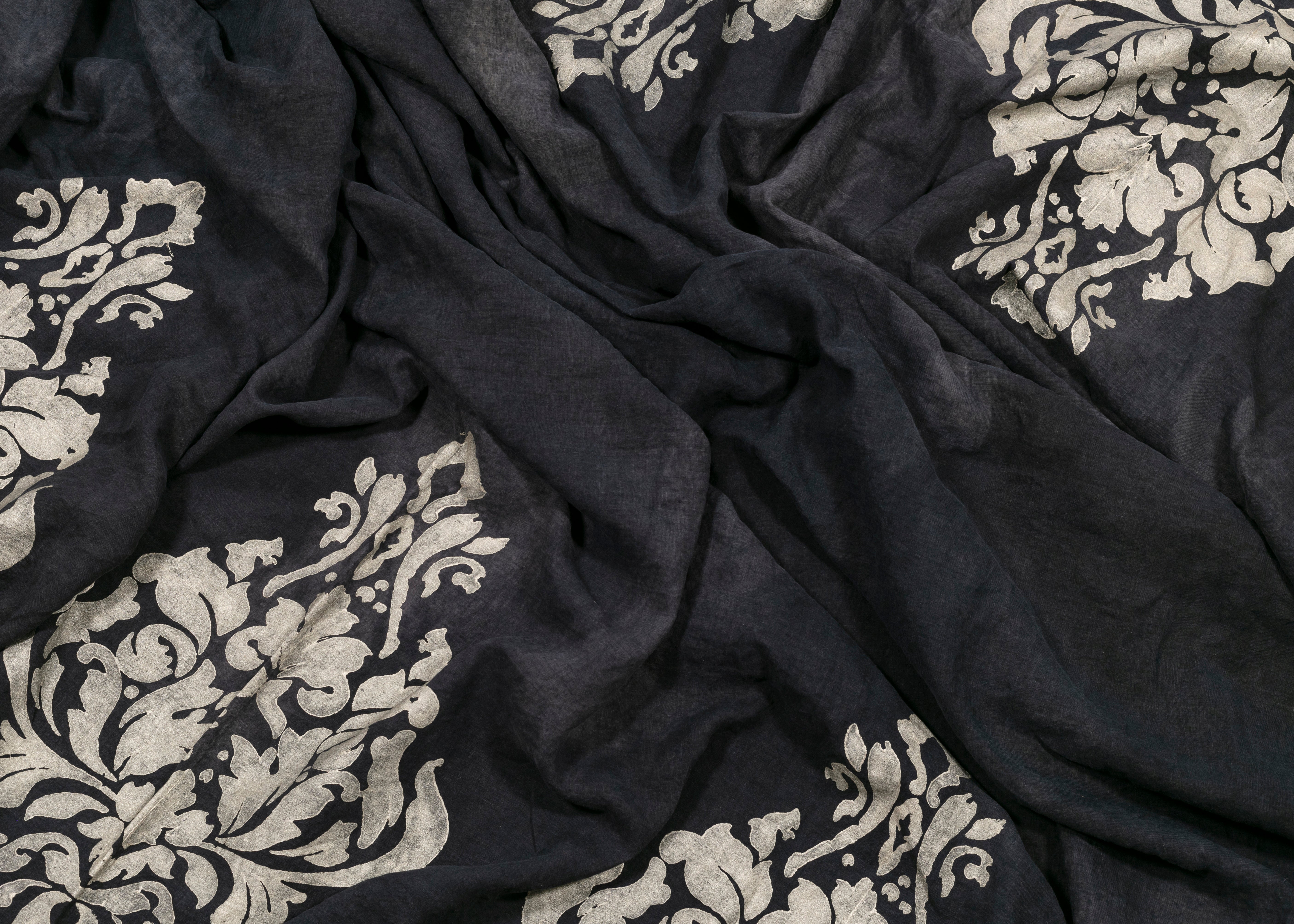 The charcoal linen of this tablecloth is complemented by champagne ornamental motifs. This striking combination adds a touch of elegance to any meal.