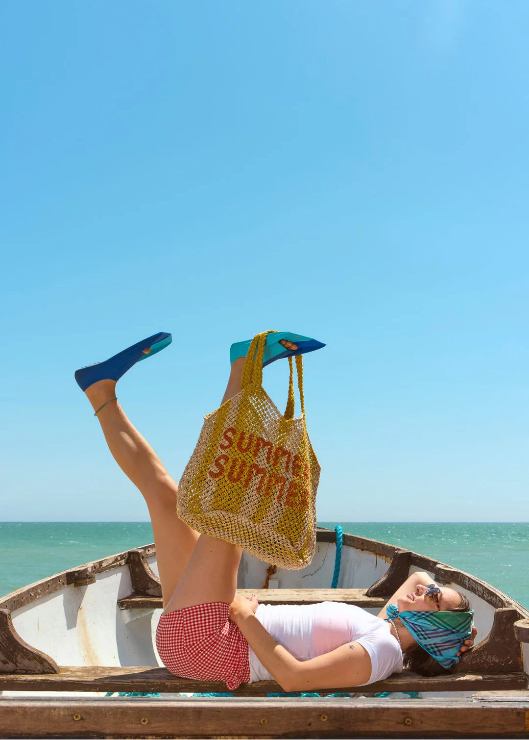 Person lying on a boat with a yellow striped 'SUMMER SUMMER' bag