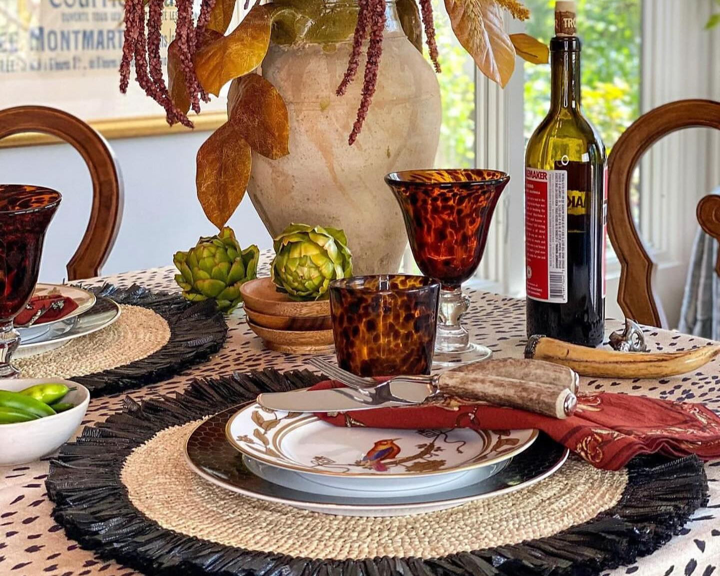 Dining table set with a floral centerpiece, wine bottle, and decorative items.