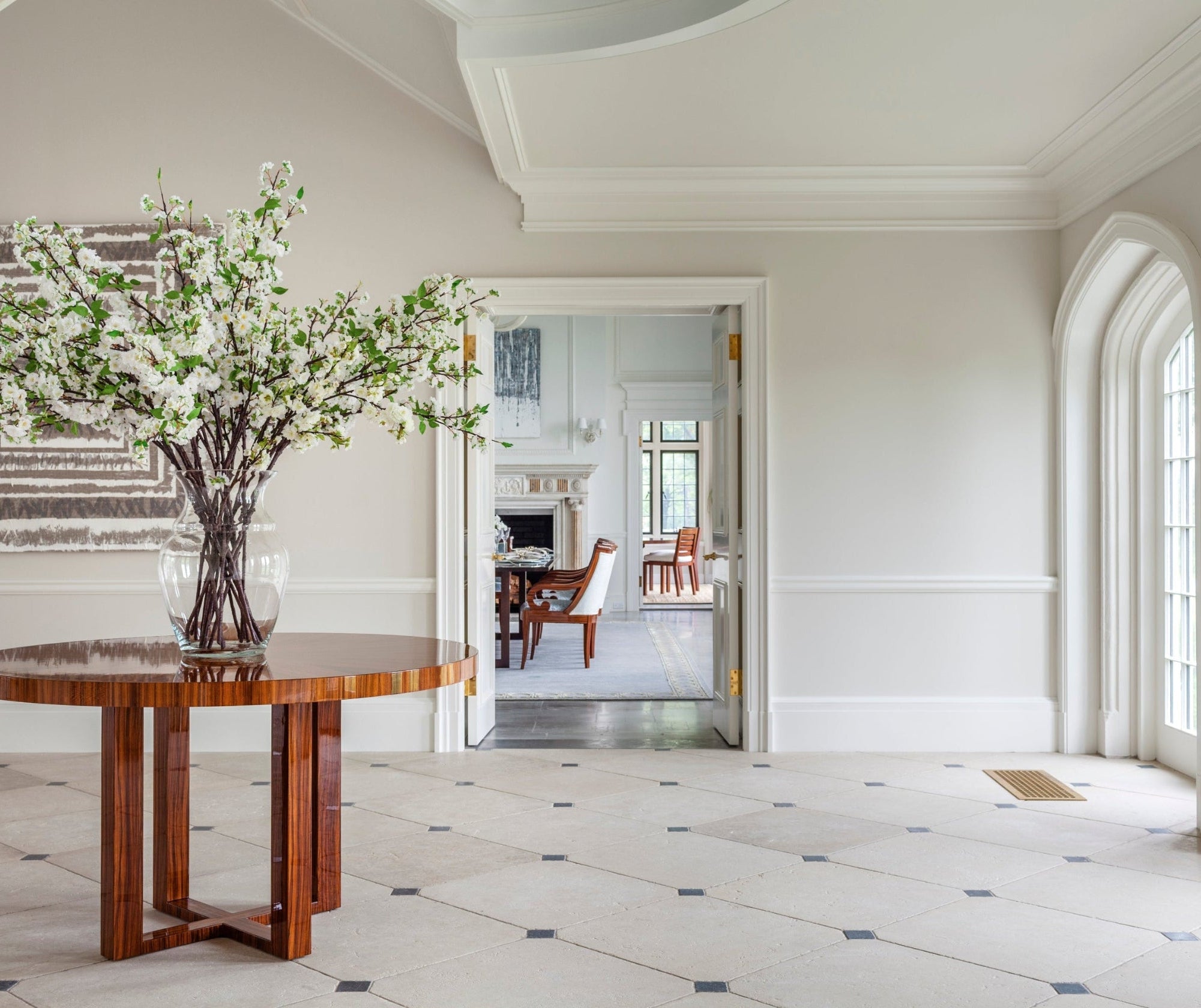 Wooden table with a vase of flowers in a room with white walls and tiled floor.