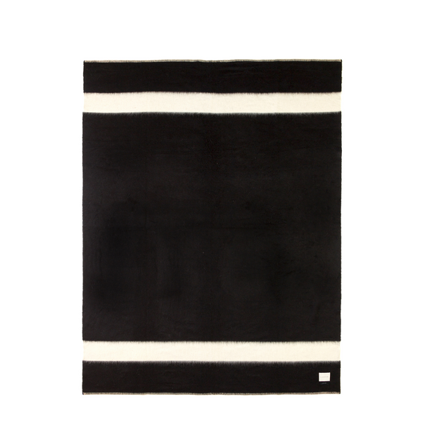 Unfolded throw reveals a classic black foundation adorned with two ivory stripes. Woven from 100% recycled fibers sourced from haute couture fashion houses, Siempre Recycled Throw blends luxury and environmental responsibility.