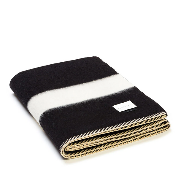The folded Siempre Recycled Throw features a black base with refined ivory stripes, embodying both sustainability and sophistication in its design.