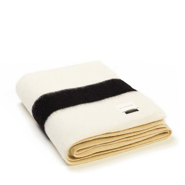 The folded Siempre Recycled Throw features an ivory foundation with bold black stripes, embodying both sustainability and classic elegance in its design.