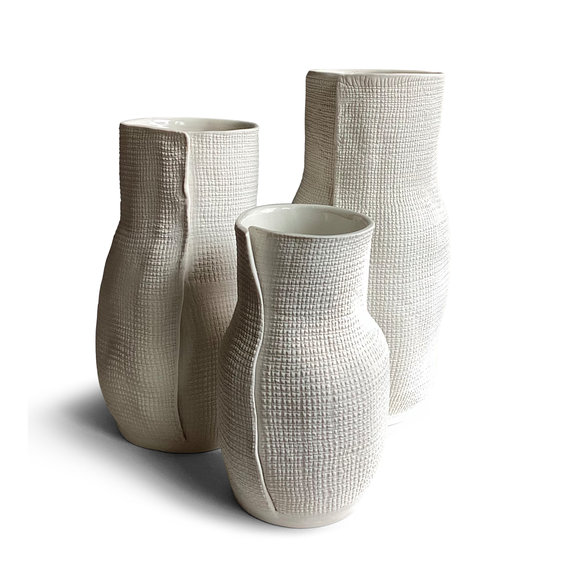 Three textured white vases of varying heights are displayed side by side, each featuring a unique, bottle-like shape, narrowing at the top. The vases have a woven-like surface pattern that adds visual interest and a tactile feel. Their modern, sculptural design makes them perfect for minimalist or contemporary decor.