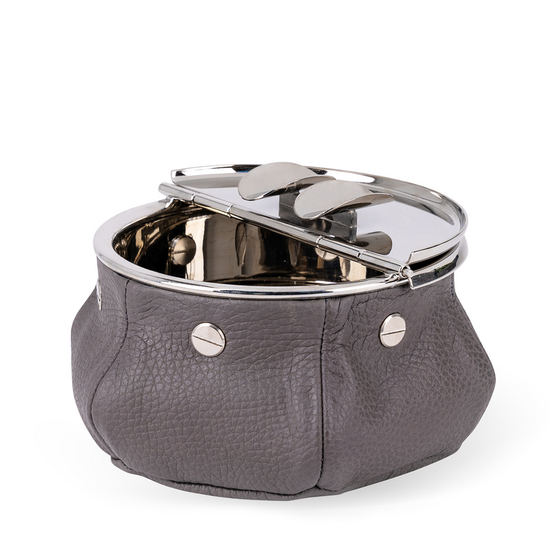 This windproof ashtray features a metal container that collects ashes, a metal lid containing the ashes, and cigar (or cigarette) holders underneath. Luxuriously covered in grey leather, it makes a functional and decorative piece for any space.