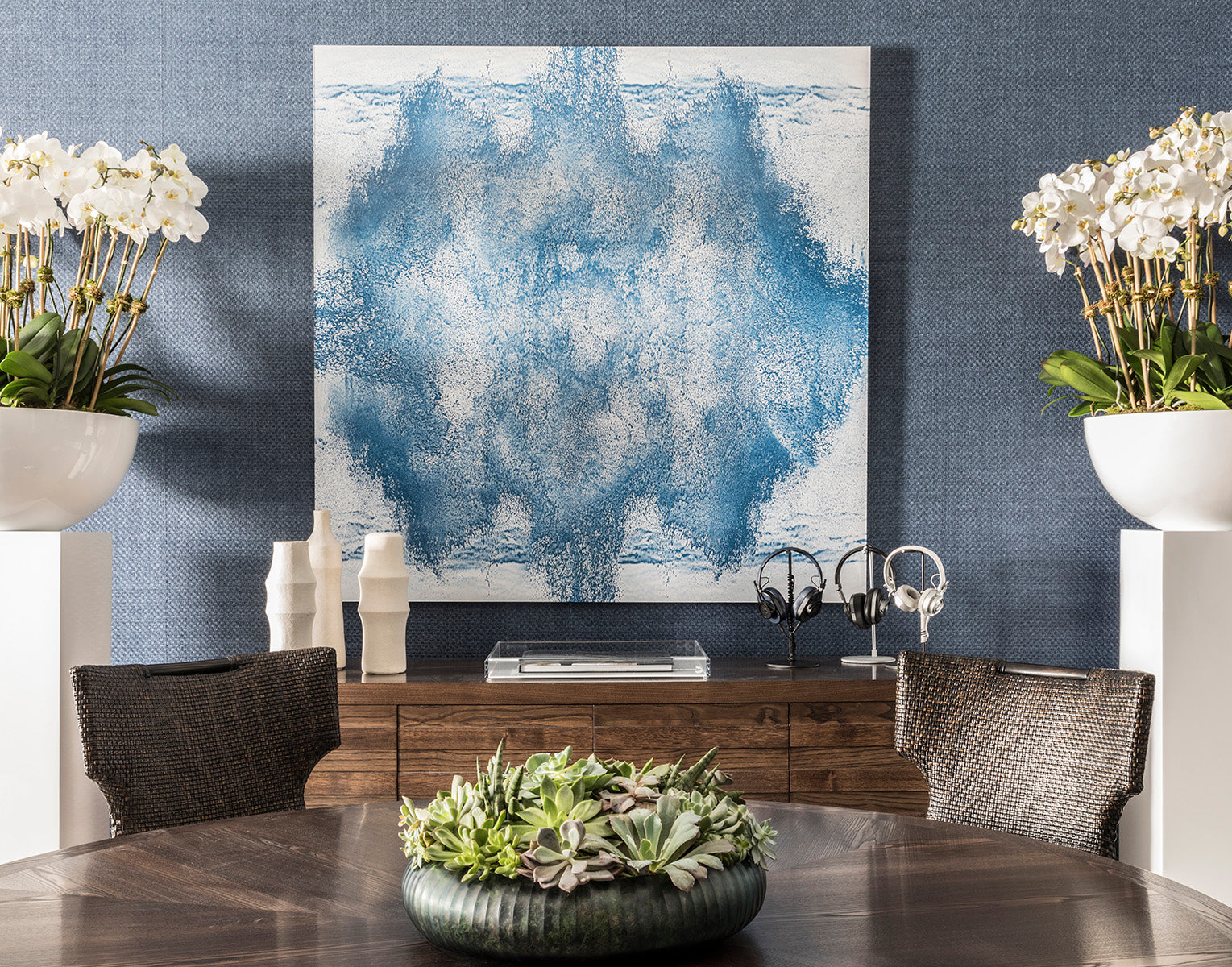 Modern interior with abstract art, plants, and furniture against a blue wall.