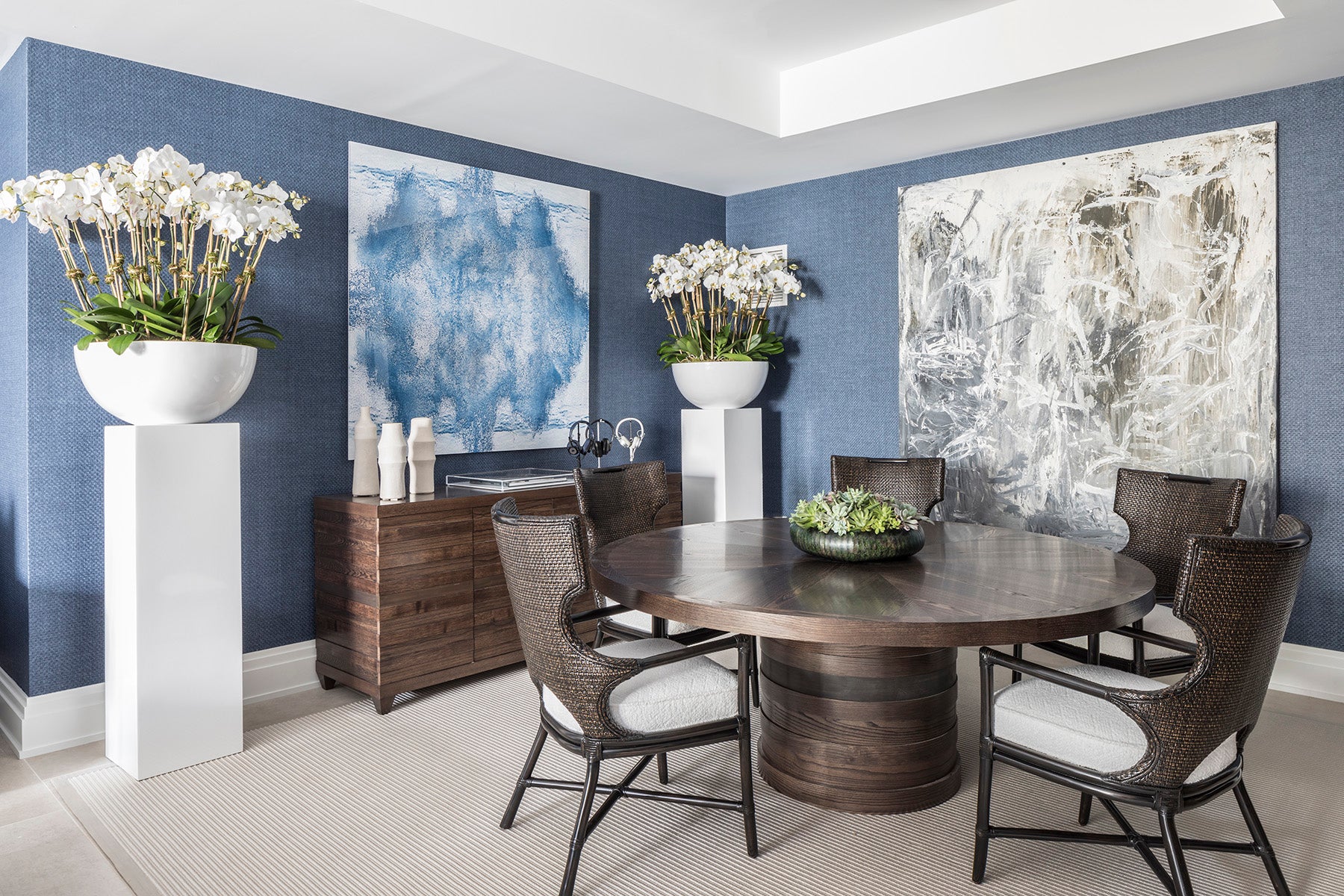 Dining room with round wooden table, chairs, and abstract wall art.