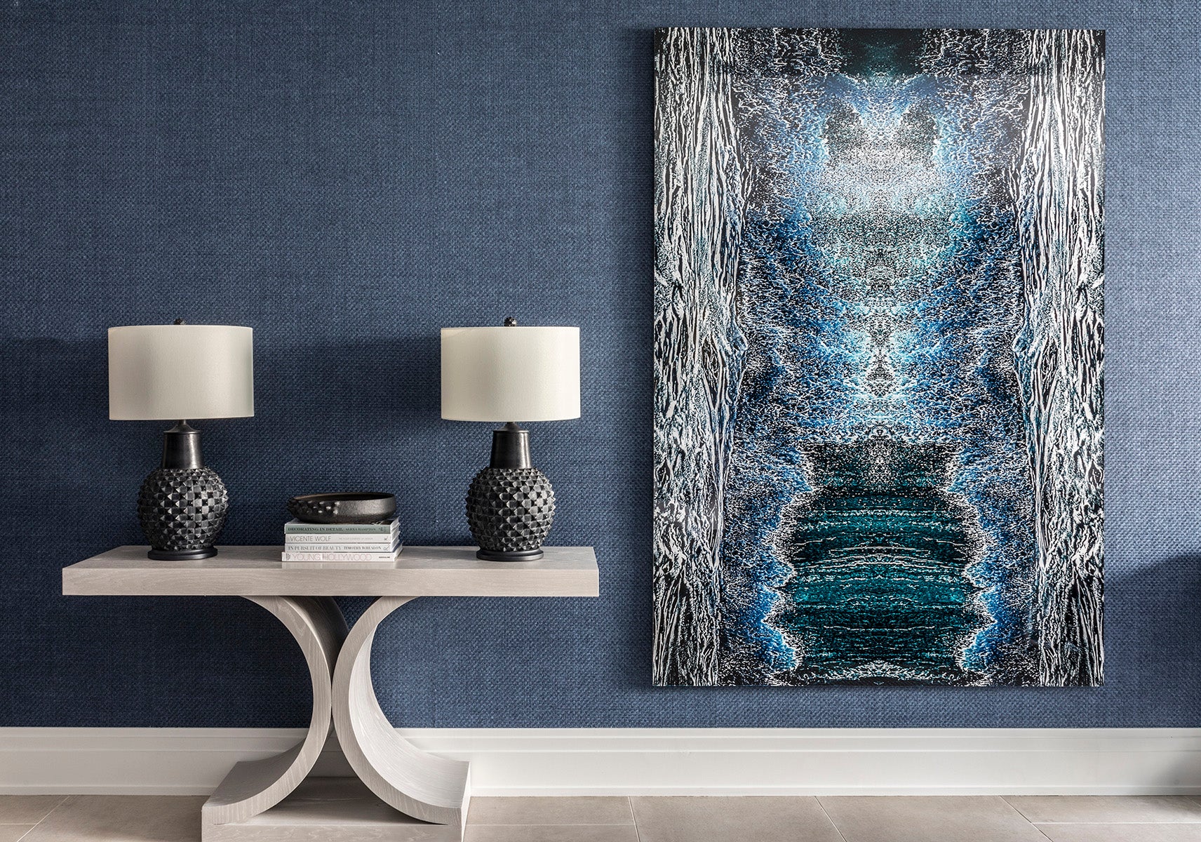 Abstract art piece on a wall with two lamps and a small table below.